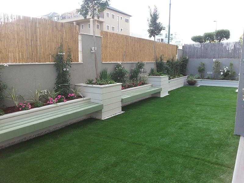 דשא סינטתי עם ספסלים ואדניות מובנות בגינת חצר