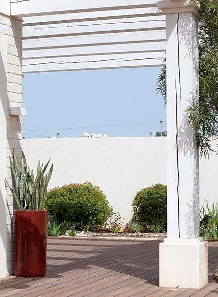 הקמת פרגולות - עיצוב גינה עם רצפת דק עץ פרגולה ועציץ גבוה אדום בחצר הבית