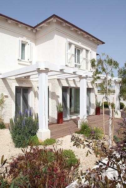 פרגולת עץ לבנה בגינת חצר שילוב צמחייה מעורבת וכדי שתילה דקורטיביים