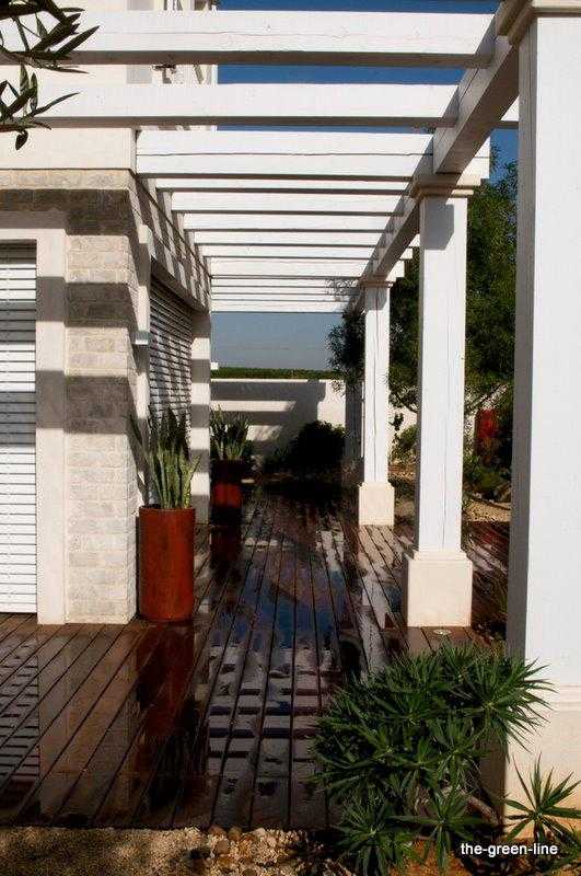 הקמת פרגולות - פרגולה לבנה בחצר הבית עם עציצים דקורטיביים גבוהים בצבע אדום