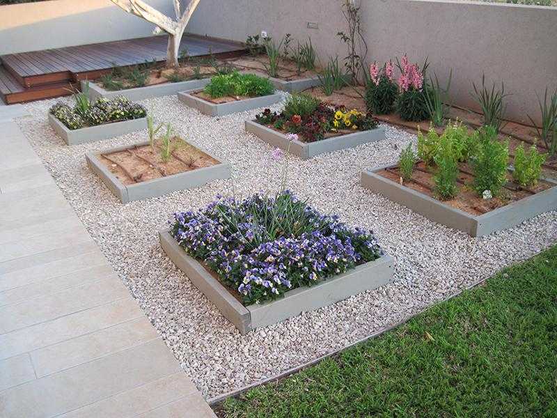 במת דק עץ בגינת חצר בשילוב חצץ עם אדניות מוגבהות ודשא