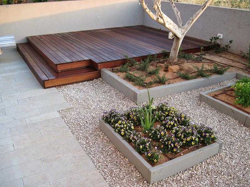 במת דק עץ בגינת חצר בשילוב חצץ עם אדניות מוגבהות