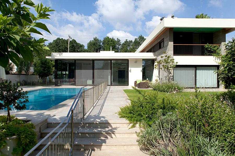 גינת חצר מעוצבת מסביב לבריכה משלבת דשא, עצים וצמחייה מעורבת