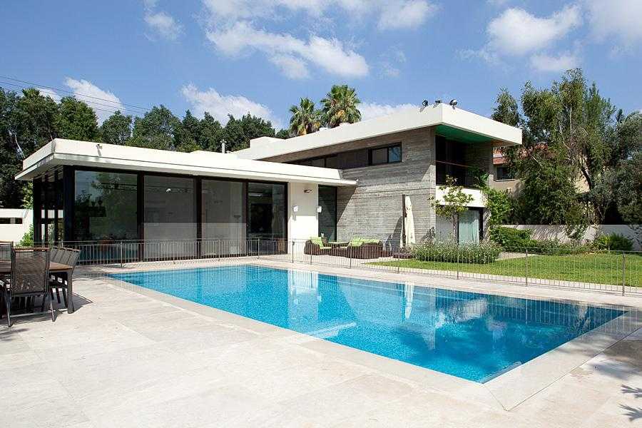 גינת חצר מעוצבת מסביב לבריכה משלבת דשא, עצים וצמחייה מעורבת