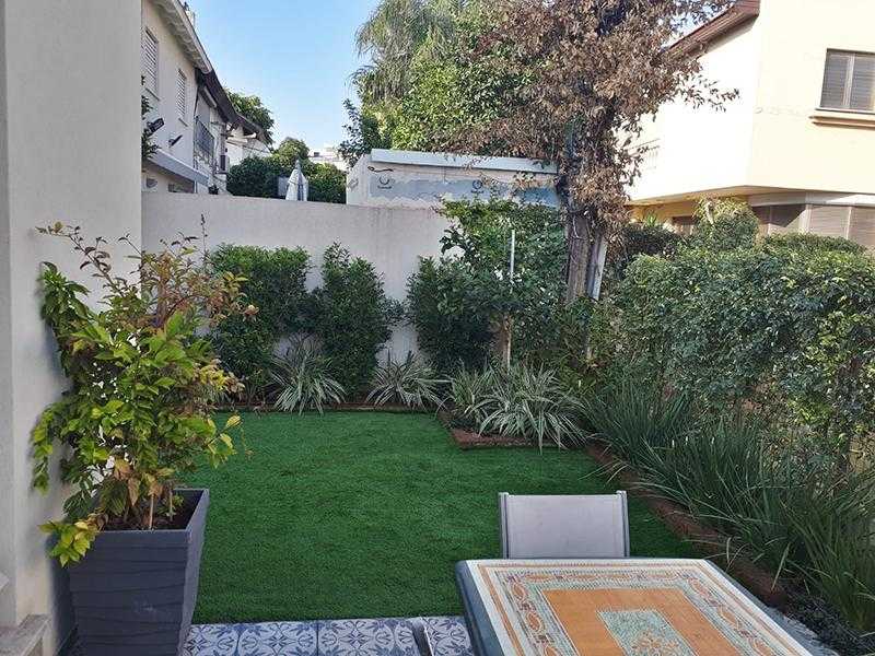 שילוב של דשא עצים אדניות כדים וצמחייה מעורבת בגינת חצר במרכז הארץ