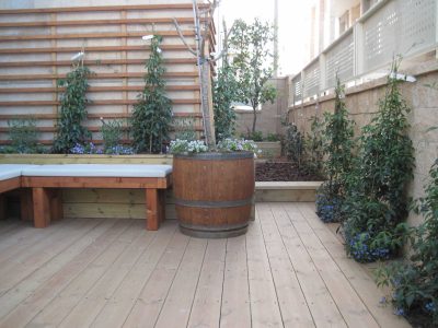 פינת ספסלי ישיבה בגינה עם עציץ ענק מעוצב ואדניות מוגבהות מסביב